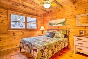 Een knus slaapkamer in een houten hutje, met een bed, nachtkastje, lamp en een raam met uitzicht.