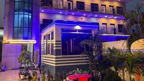 Ein mehrstöckiges Gebäude mit Balkon, Außenbereich mit Tischen und Stühlen sowie Blumentöpfen.