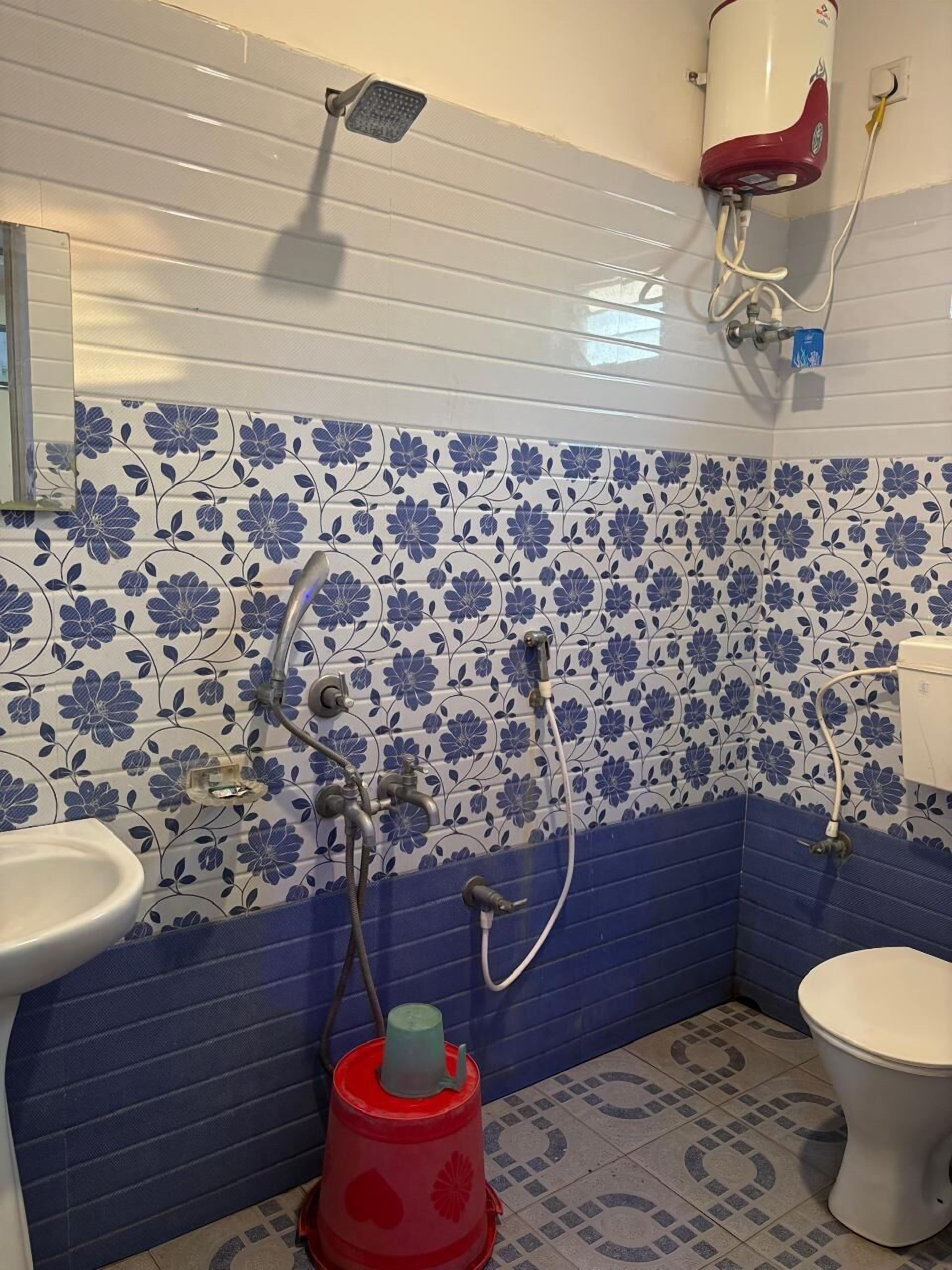 A bathroom with a shower, toilet, sink, and a red bucket.