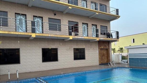 Ein Schwimmbad mit Holzterrasse, ein Gebäude mit mehreren Balkonen und eine große Holztür.