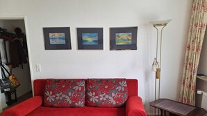 A red sofa with floral cushions, a small table, and three framed paintings on the wall. - Central vacation apartment Norderney (Norderney)