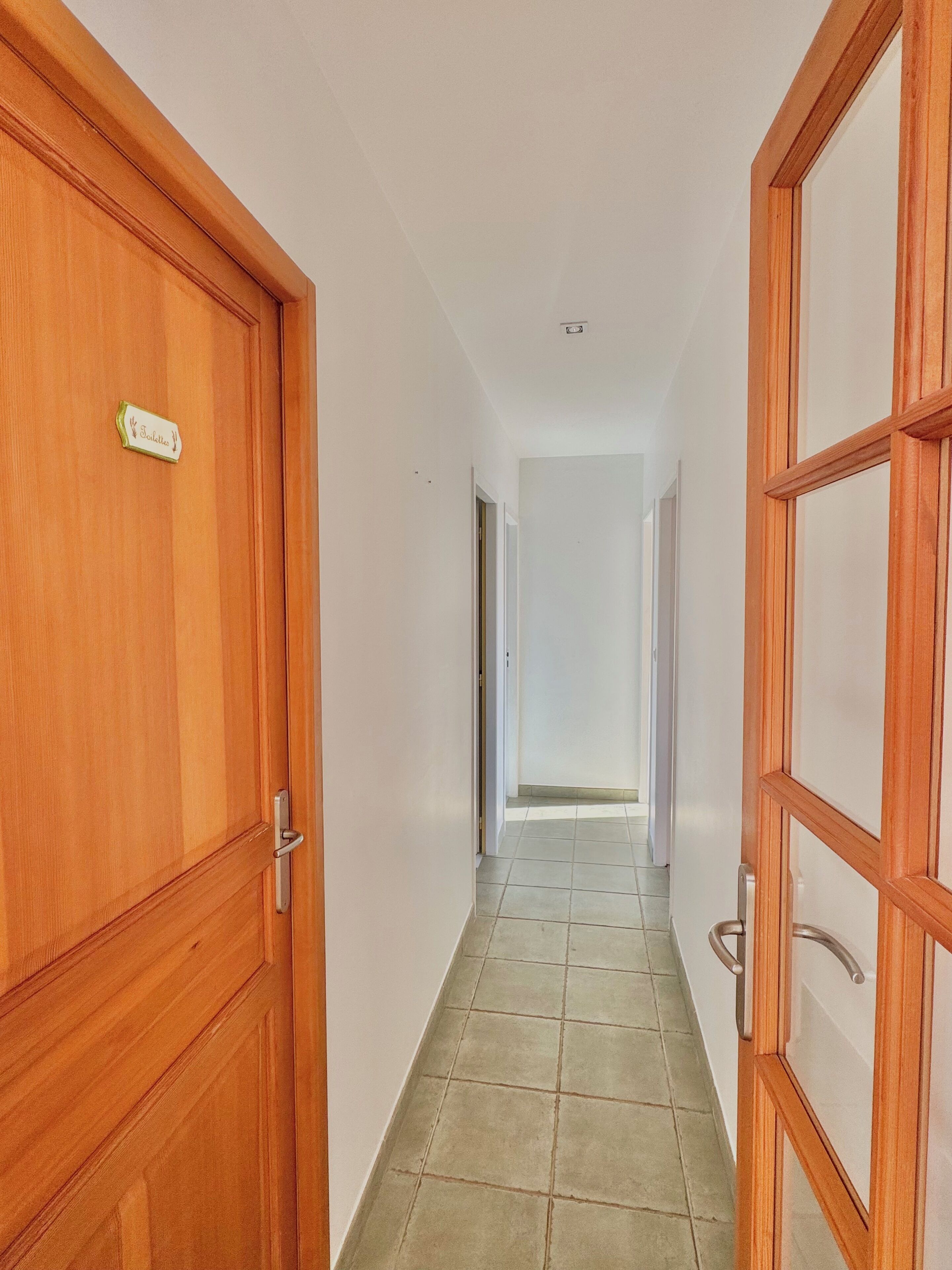 Un corridoio con porte in legno e pavimento piastrellato.