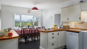 A modern kitchen with a central island, white cabinetry, and a view of the outdoors. - Eisteddfa Country House and Cottages (Criccieth)