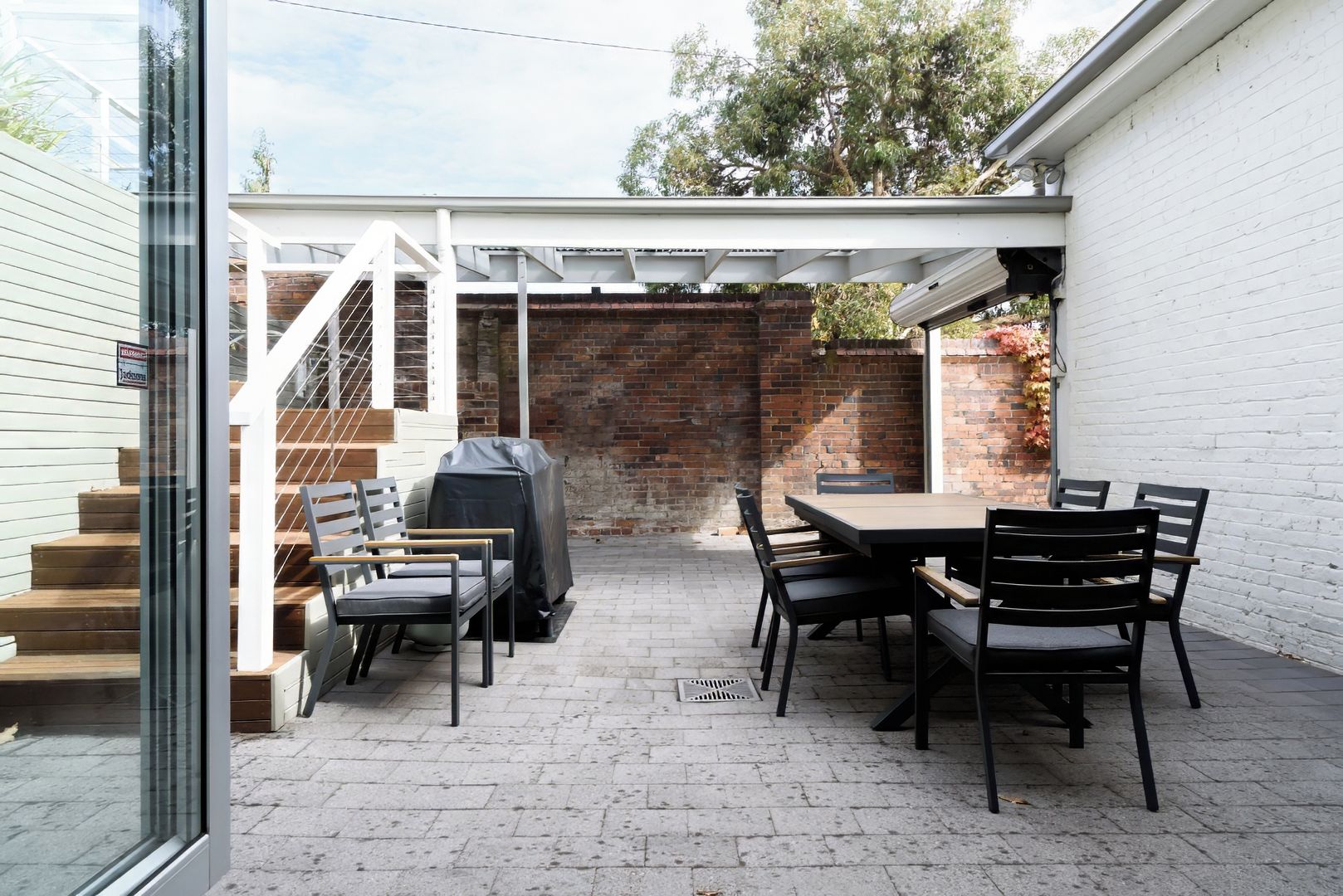 Un patio con muro de ladrillo, una parrilla cubierta y una mesa con sillas.