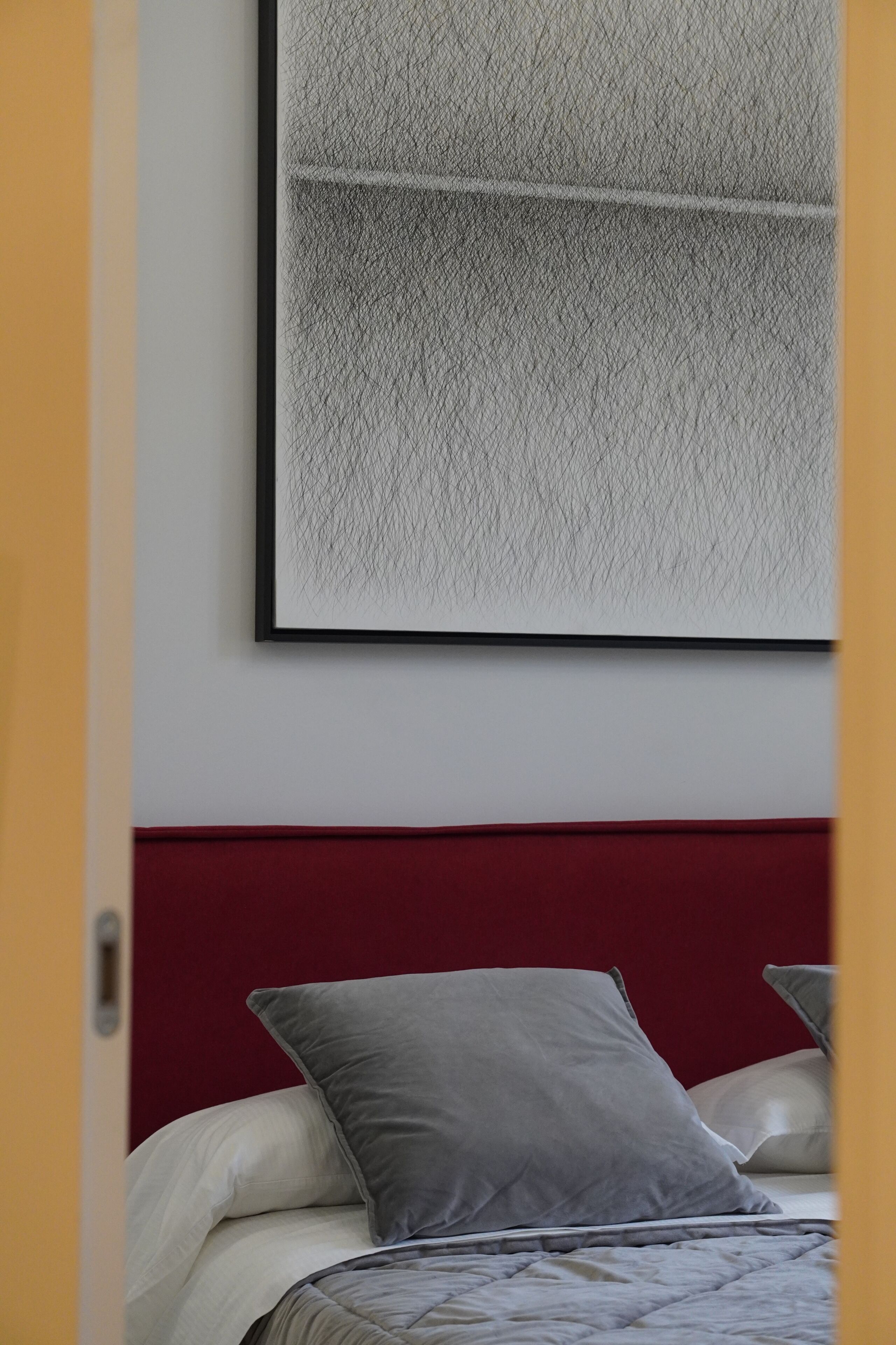A bed with a red headboard, a grey pillow, and a white blanket.