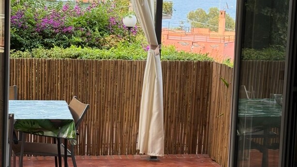 A balcony with a view of the sea, a bamboo fence, and a table with a chair. - Terrace Garden Apartment (Aci Trezza)