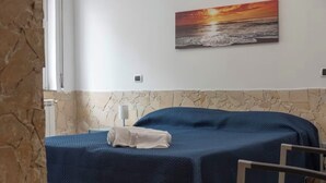 A bedroom with a bed, a nightstand, a chair, and a painting of a sunset over the ocean. - Terrace Garden Apartment (Aci Trezza)