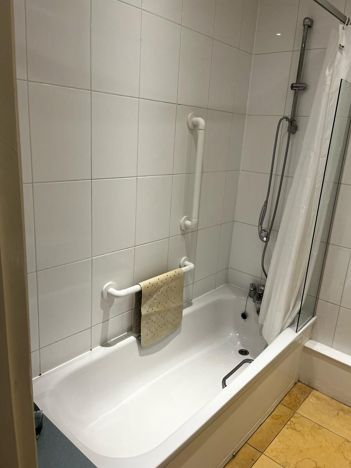 Un baño moderno con una bañera blanca, cabina de ducha con mampara de vidrio y un perchero con toalla.