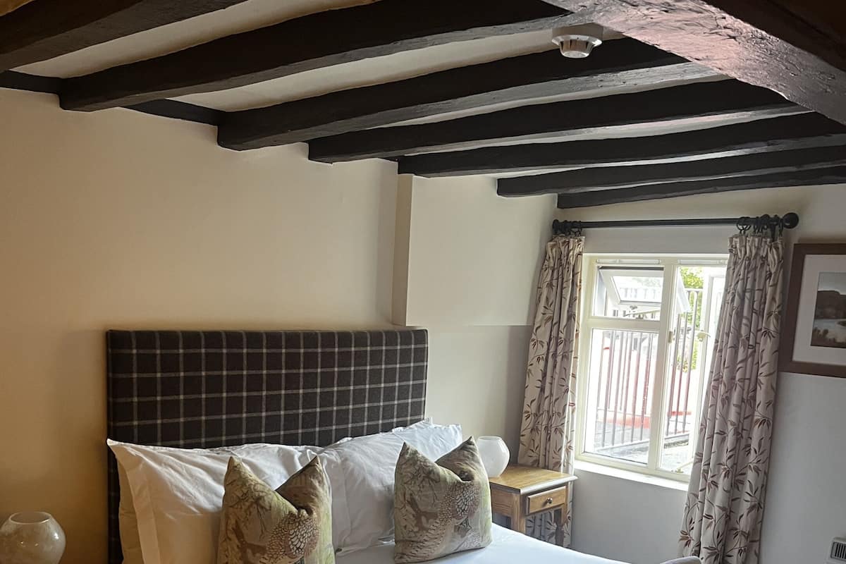 A hotel room with a bed, pillows, a bedside table, a lamp, and a window with curtains.