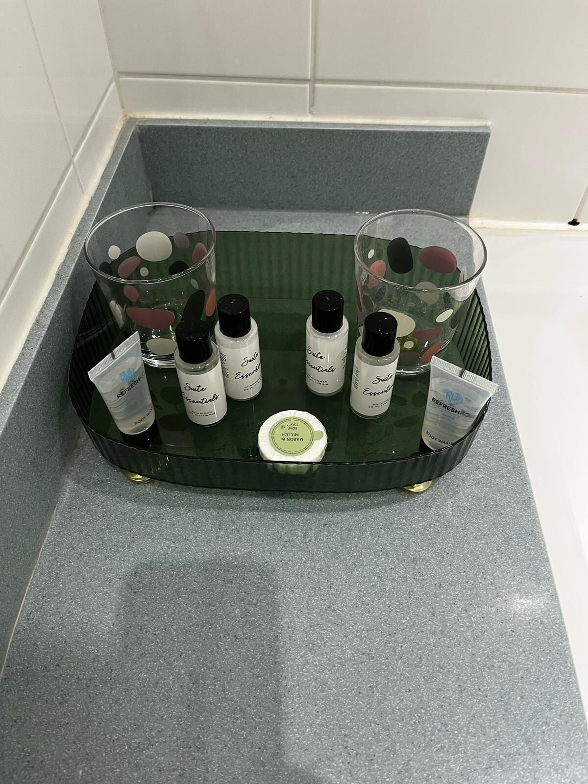 Ein Badezimmer-Waschtisch mit einer grünen Ablage, auf der verschiedene Pflegeprodukte und ein Glas Wasser stehen.