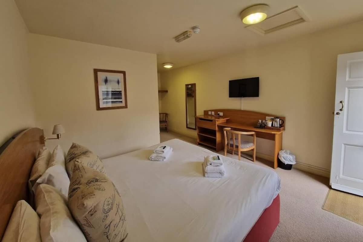 A hotel room with a bed, a desk, a chair, a television, and a door.