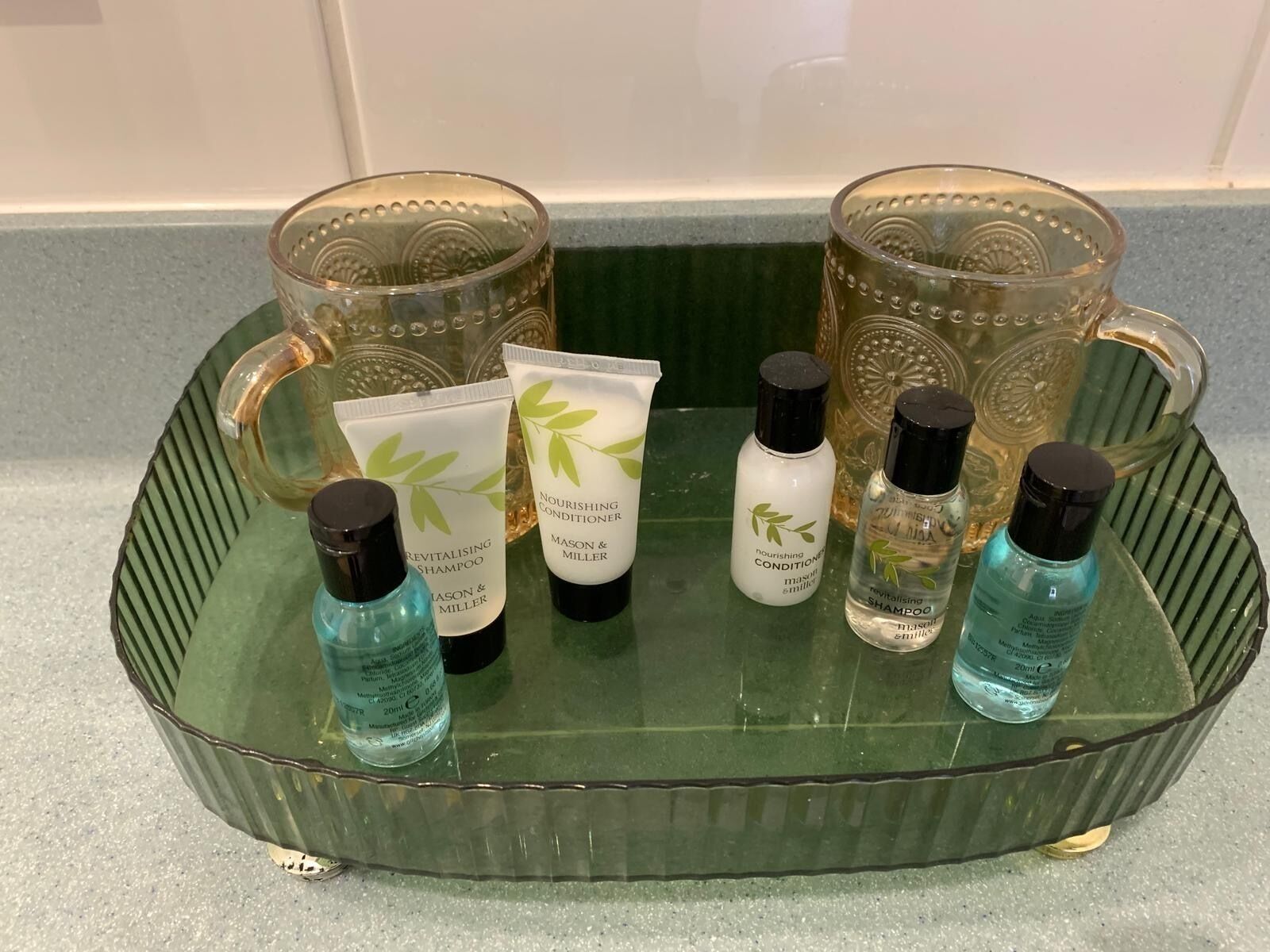 Een glazen dienblad met diverse persoonlijke verzorgingsproducten, zoals shampoos en conditioners, op een aanrecht.