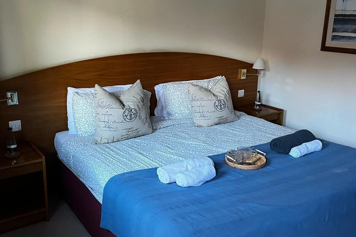 A neatly made bed with a blue blanket, white pillows with text, and a framed picture on the wall.