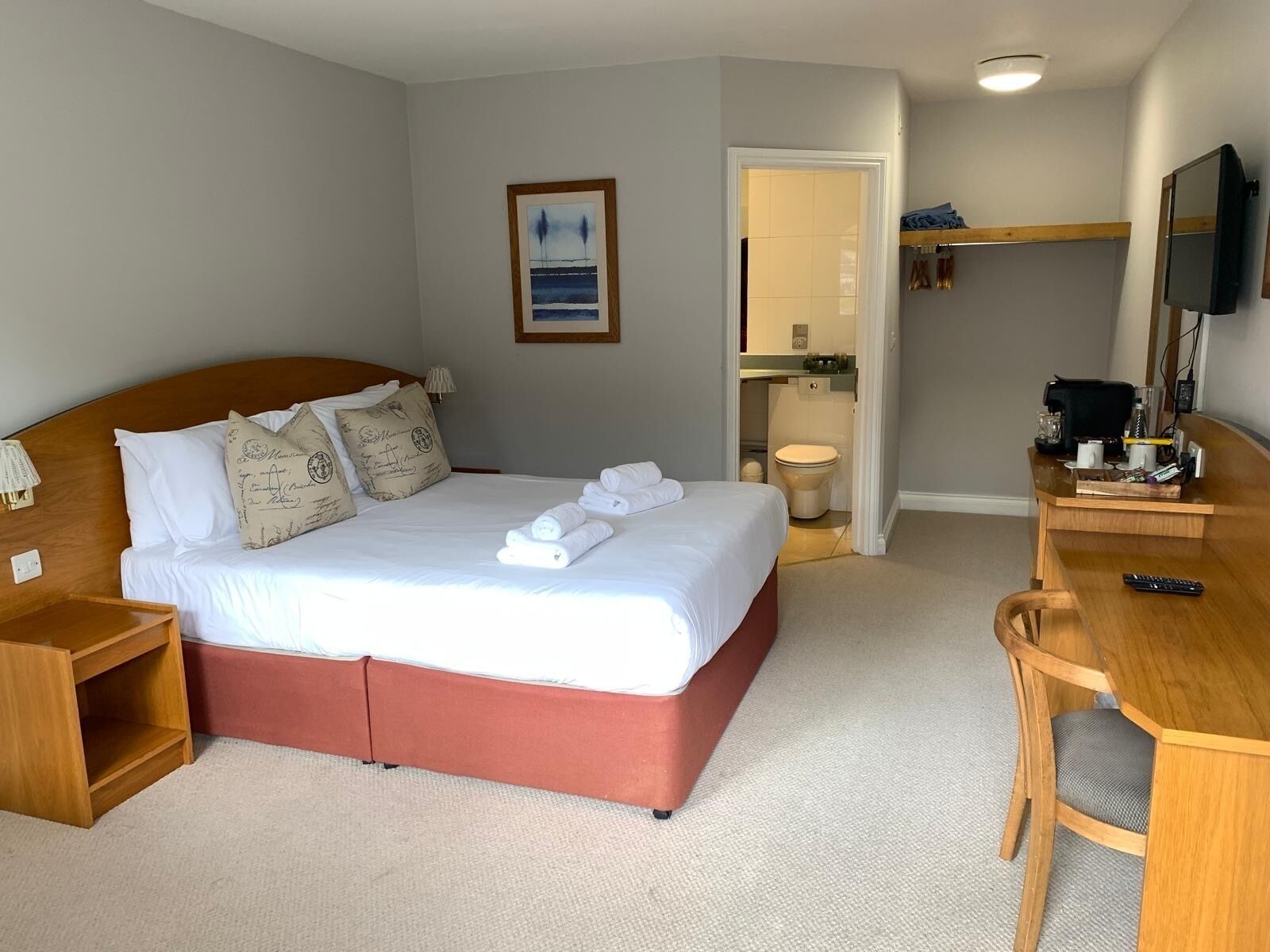 A hotel room with a bed, a desk, a chair, a television, and a bathroom visible through an open door.