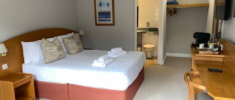 A hotel room with a bed, a desk, a chair, a television, and a bathroom visible through an open door.