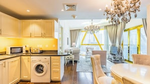 Een moderne keuken met een wasmachine, een eethoek met een kroonluchter en uitzicht op de stad door grote ramen.