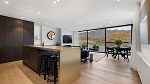 A modern kitchen with a central island, bar stools, and a large window offering a mountain view. - The Bunkers Penthouse-2 Bed (Queenstown)