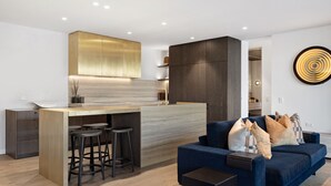A modern kitchen with a central island, bar stools, and a dark wood accent wall. - The Bunkers Penthouse-2 Bed (Queenstown)