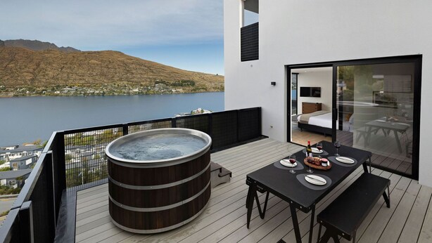 A balcony with a hot tub, dining table, and a bedroom with a bed and TV. - The Bunkers Penthouse-2 Bed (Queenstown)