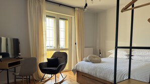 A bedroom with a bed, a desk with a TV, a rocking chair, and a large window with curtains. - House with garden near Turin & Asti – Relax in nature (Villanova d'Asti)