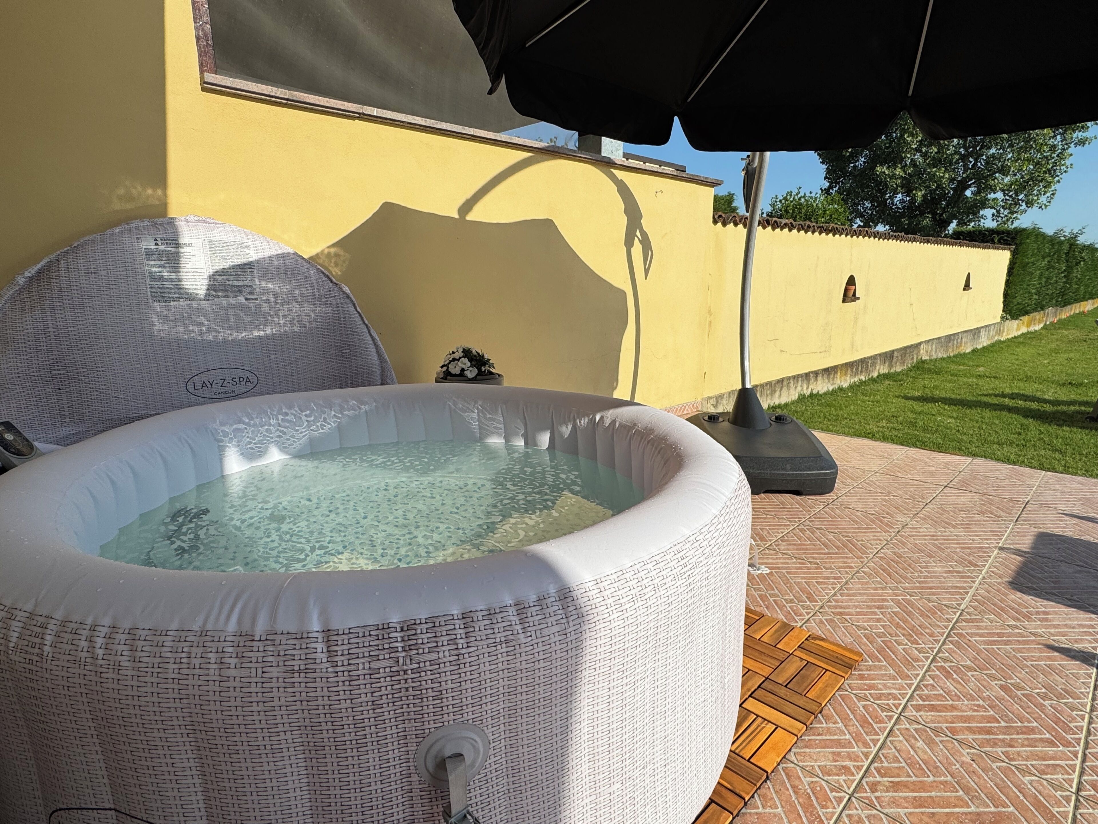 An outdoor hot tub with a textured cover, a small potted plant, and a patio umbrella.