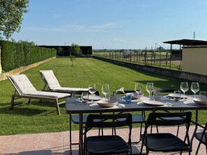 An outdoor dining area with a table set for two, surrounded by chairs, and a view of a well-maintained lawn and fence.