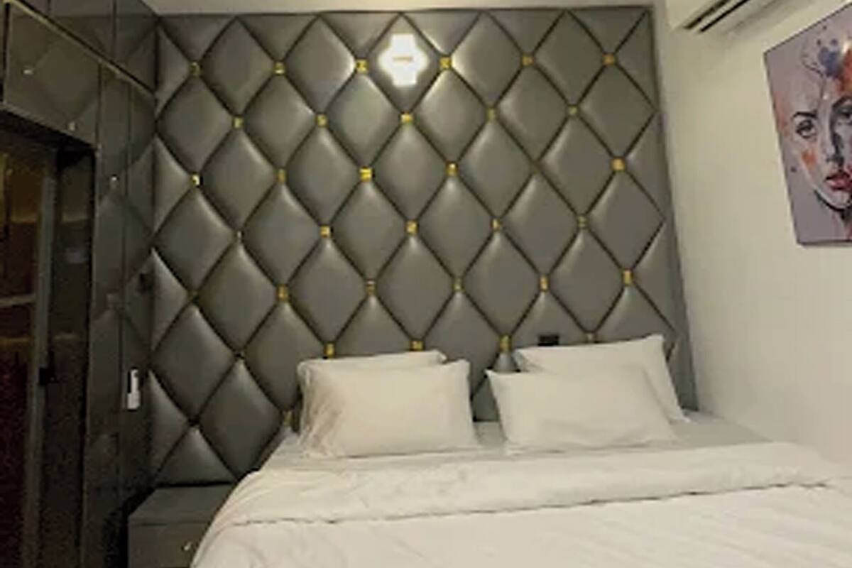 Quarto com cabeceira estofada, cama com roupa de cama branca e luz de teto embutida.