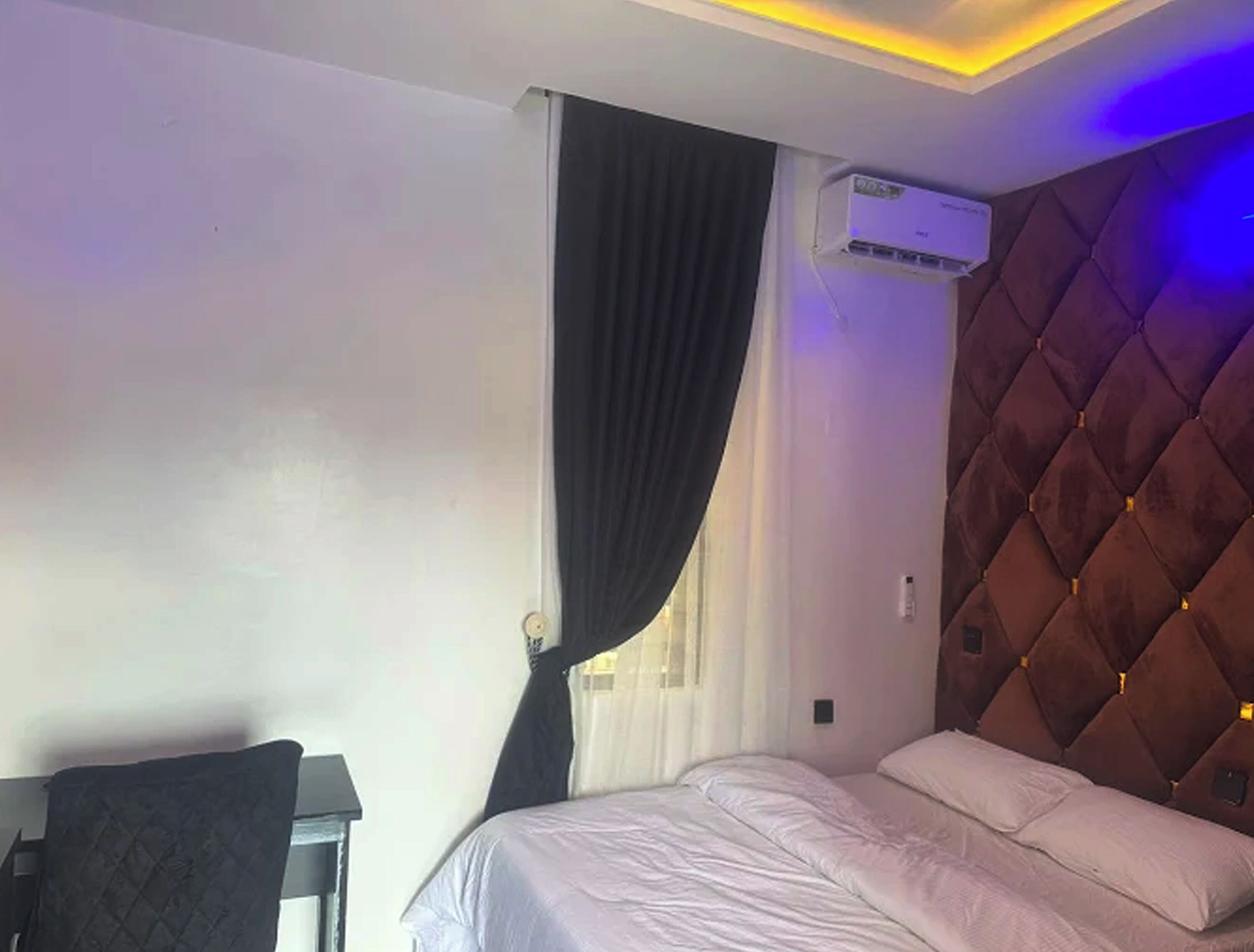 A hotel room with a bed, a desk, a chair, an air conditioning unit, and a window with curtains.
