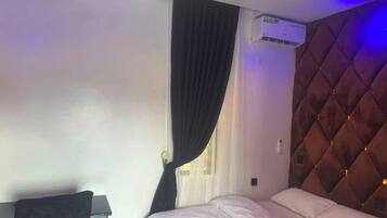 A hotel room with a bed, a desk, a chair, an air conditioning unit, and a window with curtains.
