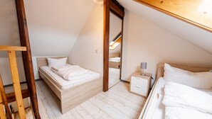 Un pequeño dormitorio en el ático, con forma de triángulo, equipado con dos camas, una mesita de noche y una escalera de madera.