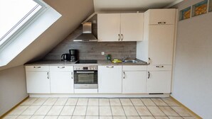 Una cocina compacta con armarios blancos, horno empotrado y cafetera sobre la encimera.