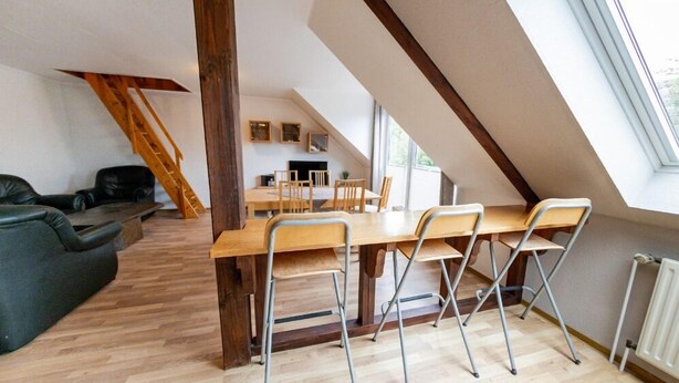 Habitación tipo loft con comedor, piso de madera y un ventanal grande que proporciona luz natural.