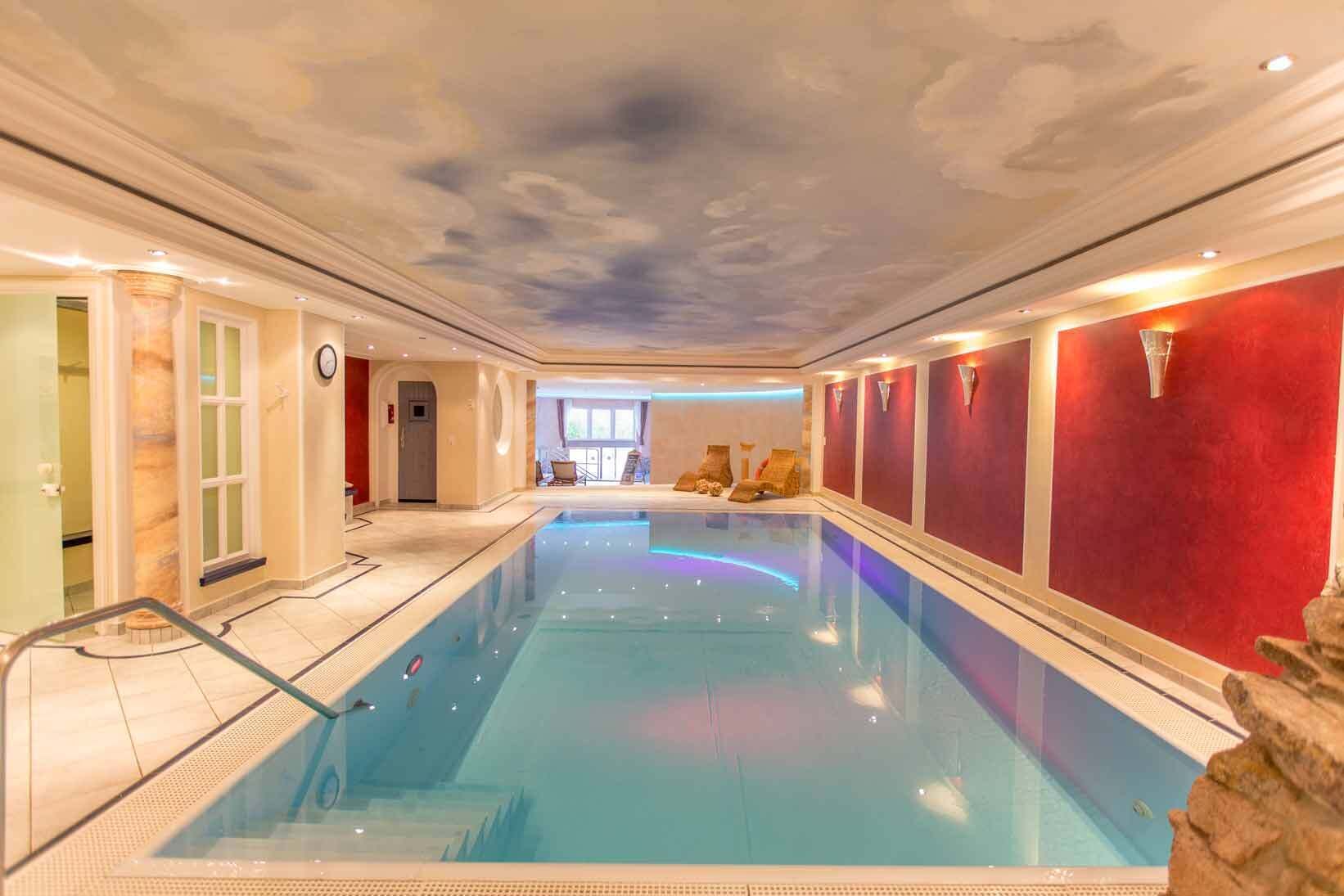 Ein Innenpool mit Deckenfresko, roten Wänden und Blick auf einen Raum mit einem Fenster.