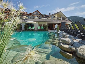 A clear pool with lounge chairs and a building with a balcony. - Hotel Heselbacher Hof  (Baiersbronn)