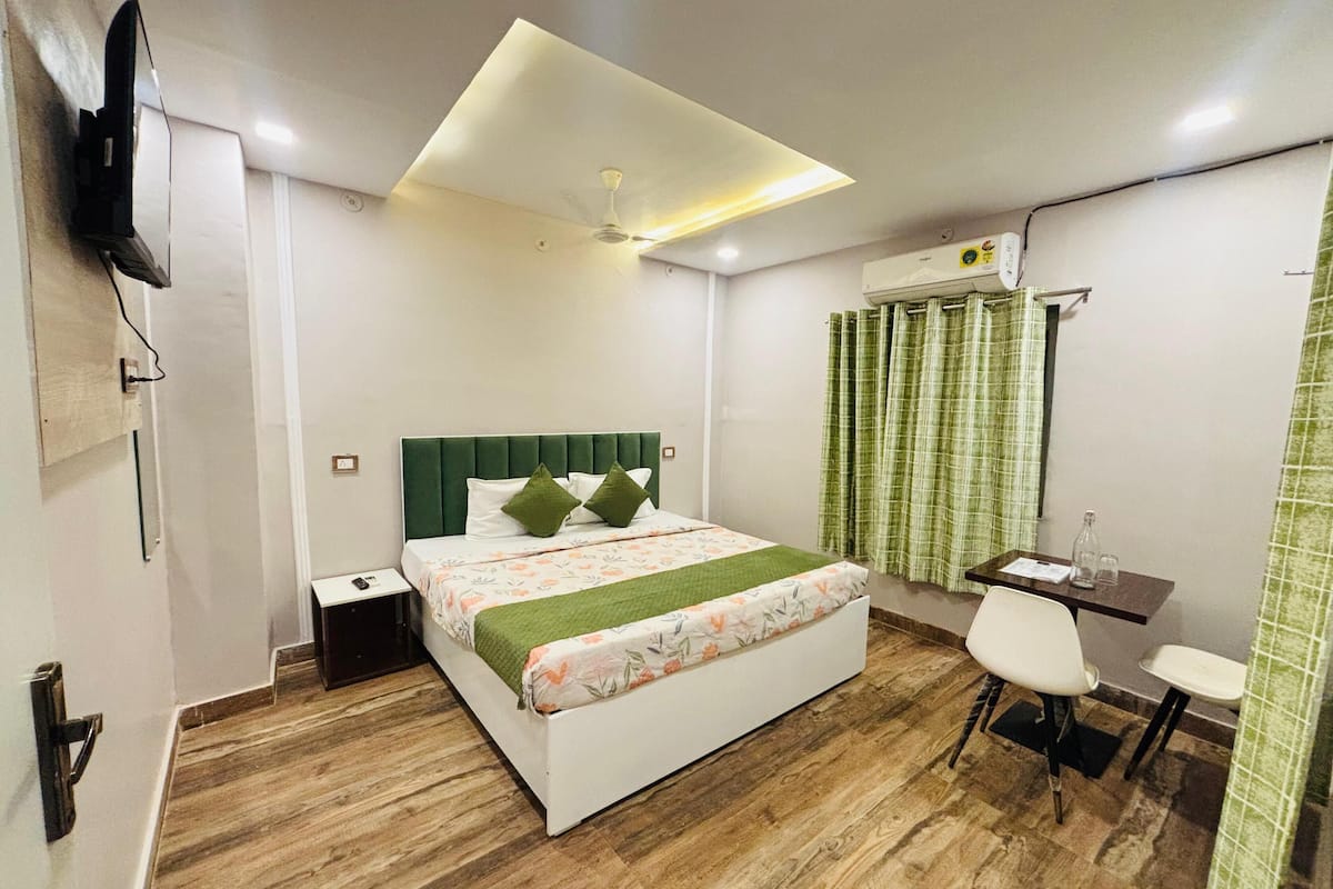 Una camera d'albergo moderna con un letto, un comodino, una scrivania, una sedia e una TV a schermo piatto fissata al muro.
