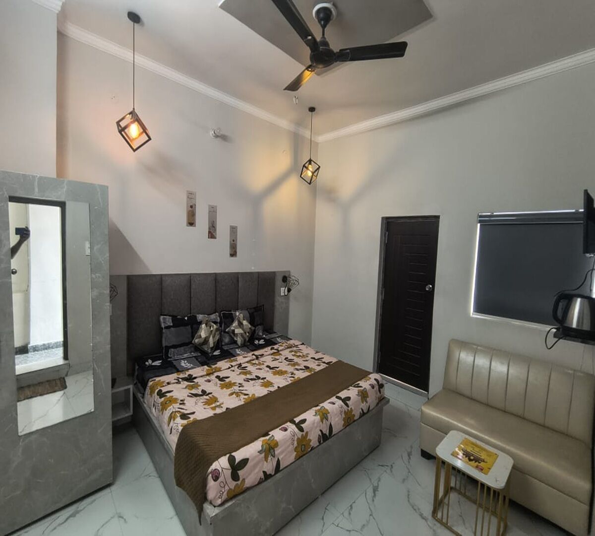 Una camera da letto con un letto, una ventola a soffitto, una TV, un tavolino e una porta.