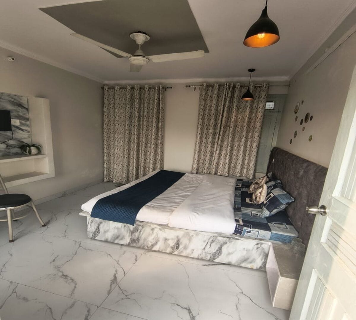 Une chambre à coucher avec un lit, des rideaux, un ventilateur de plafond et un luminaire suspendu.