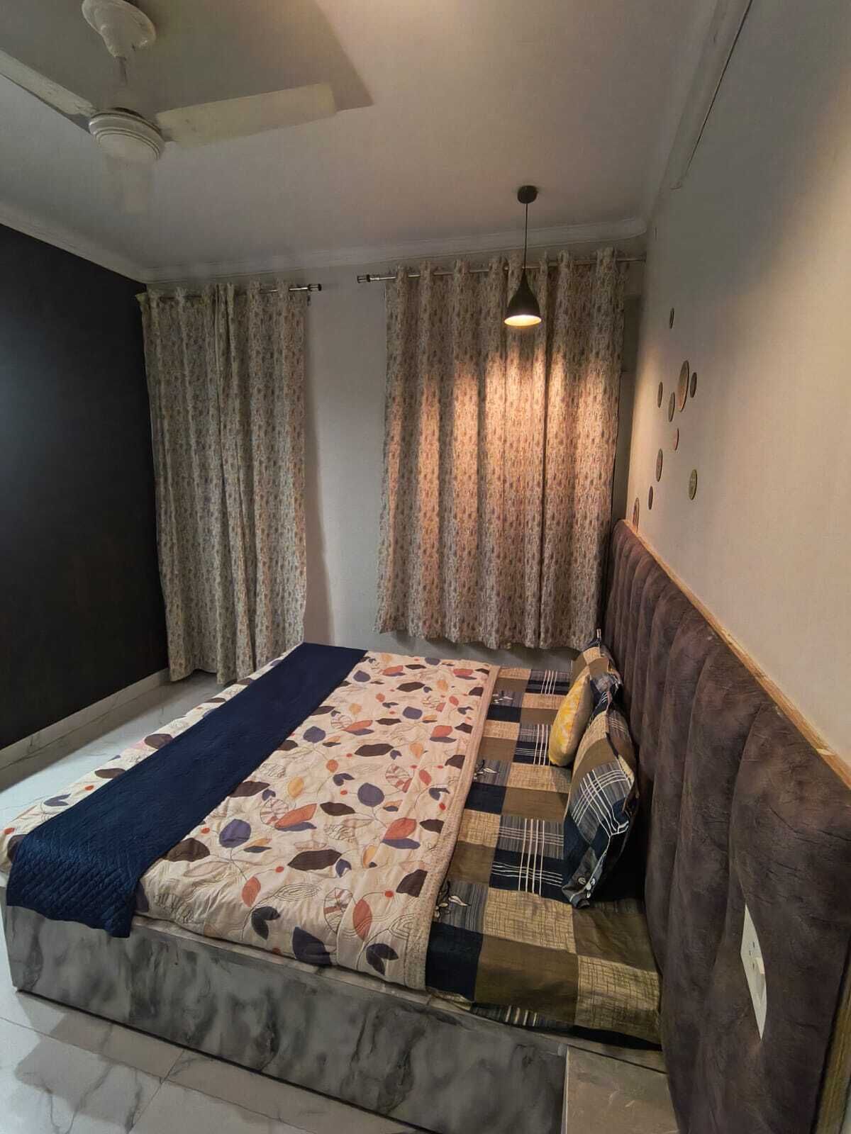 A bedroom with a bed, curtains, a ceiling fan, and a wall with decorative plates.