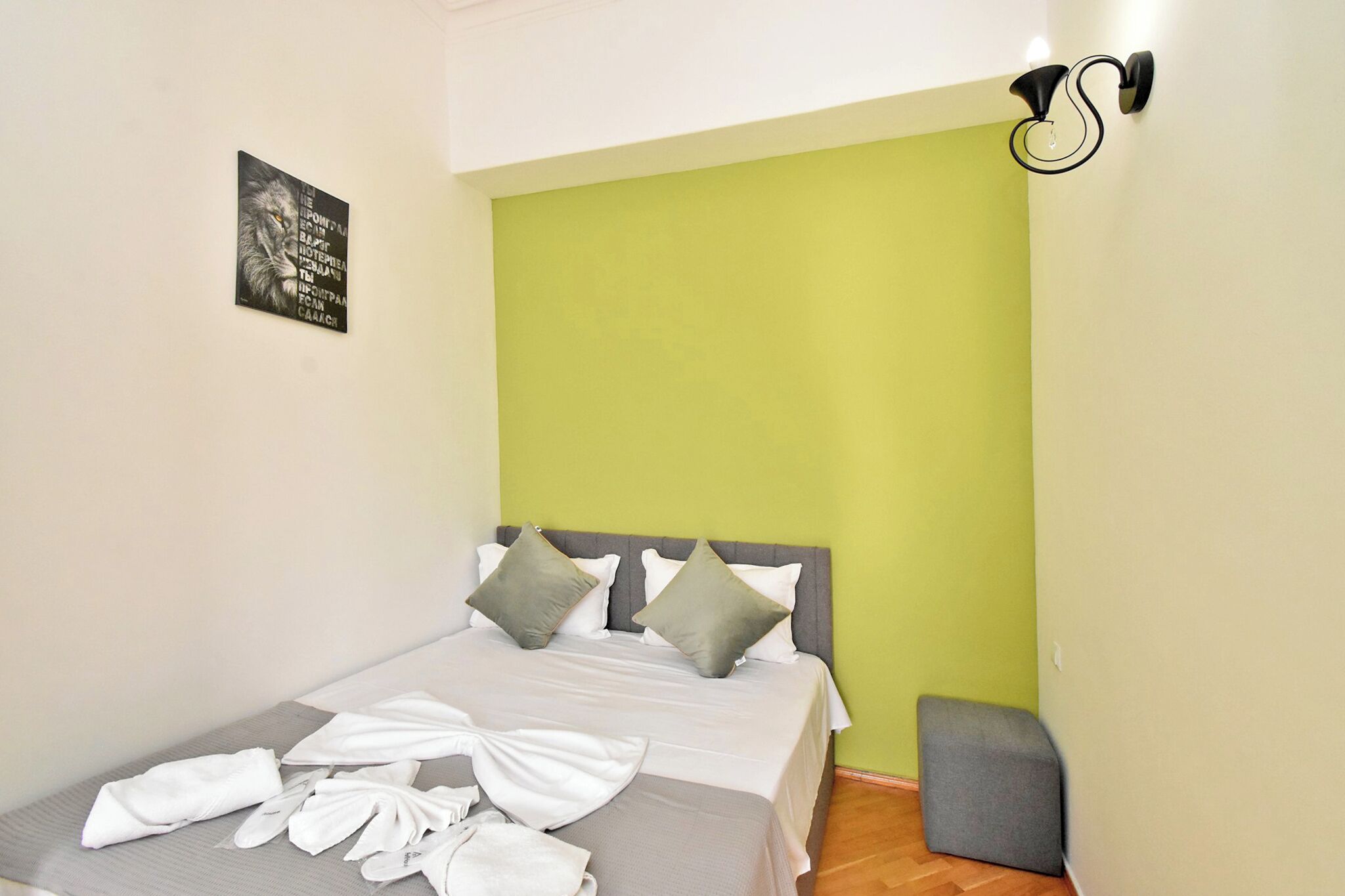 A neatly made bed with pillows, a grey headboard, and a green accent wall.