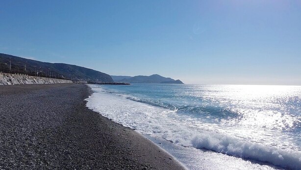 Ein Strand mit felsigem Ufer, ruhigem Meer und Bergen in der Ferne.