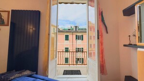 Ein Zimmer mit einem Bett, einem Fenster mit Blick auf Gebäude und einer Tür, die auf einen Balkon führt.
