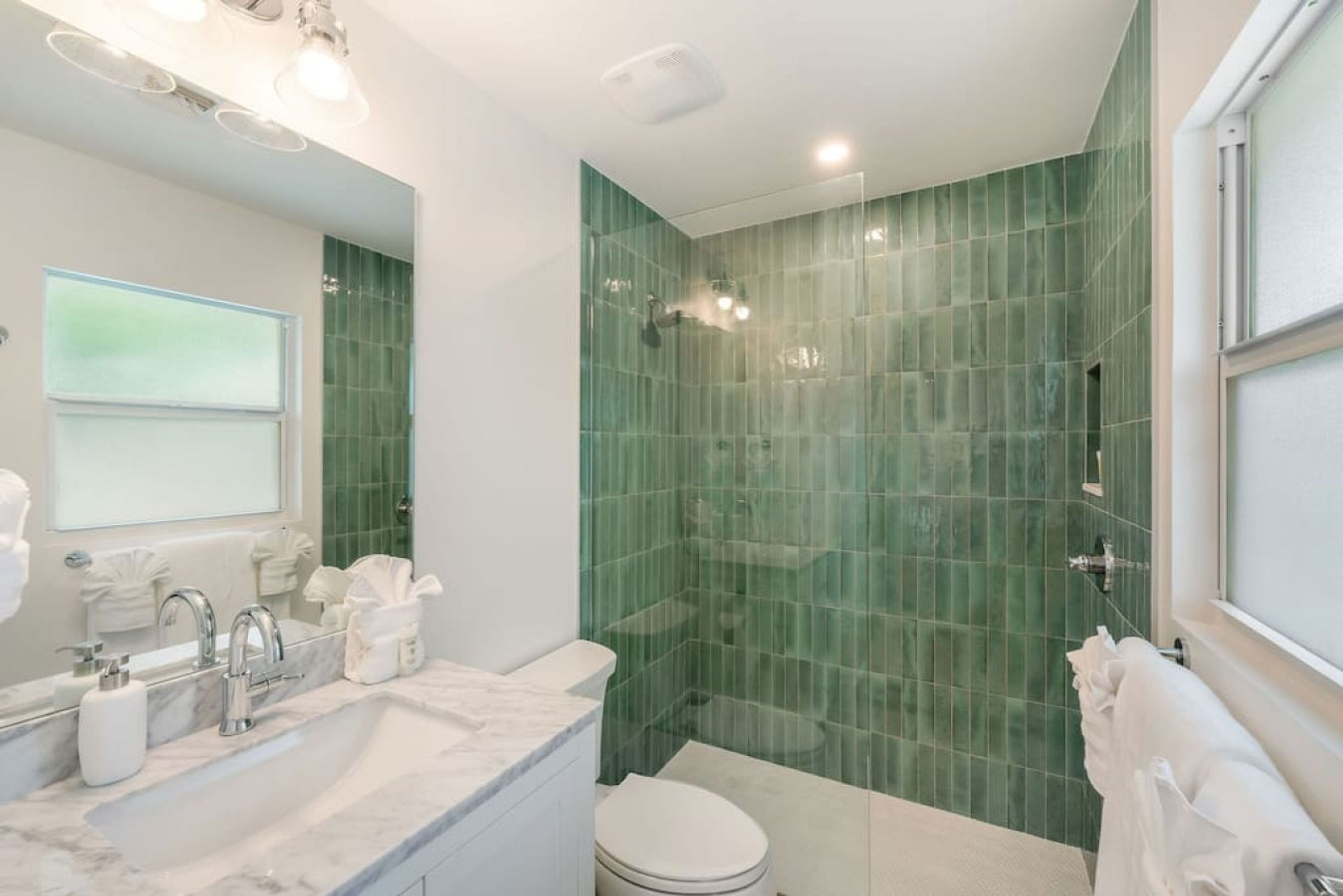A modern bathroom with a glass shower enclosure, a white sink with a marble countertop, and a toilet.