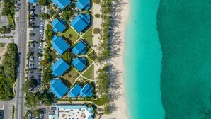 Vista aérea de un hotel costero con varios edificios de techos azules, una playa de arena y un mar turquesa cristalino.