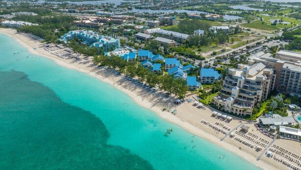 Vista aérea de un resort costero con villas frente a la playa, una playa de arena y un puerto deportivo.