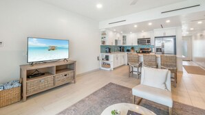 Una sala de estar moderna con televisión, muebles de mimbre y una cocina al fondo.
