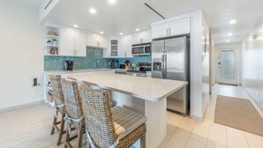 Una cocina moderna con armarios blancos, una isla grande, electrodomésticos de acero inoxidable y un salpicadero con azulejos azules.