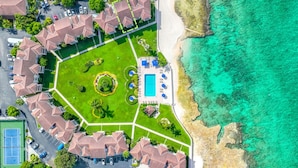 An aerial view of a resort with a pool, tennis court, and beachfront. - George Town Villas 117 (Seven Mile Beach)