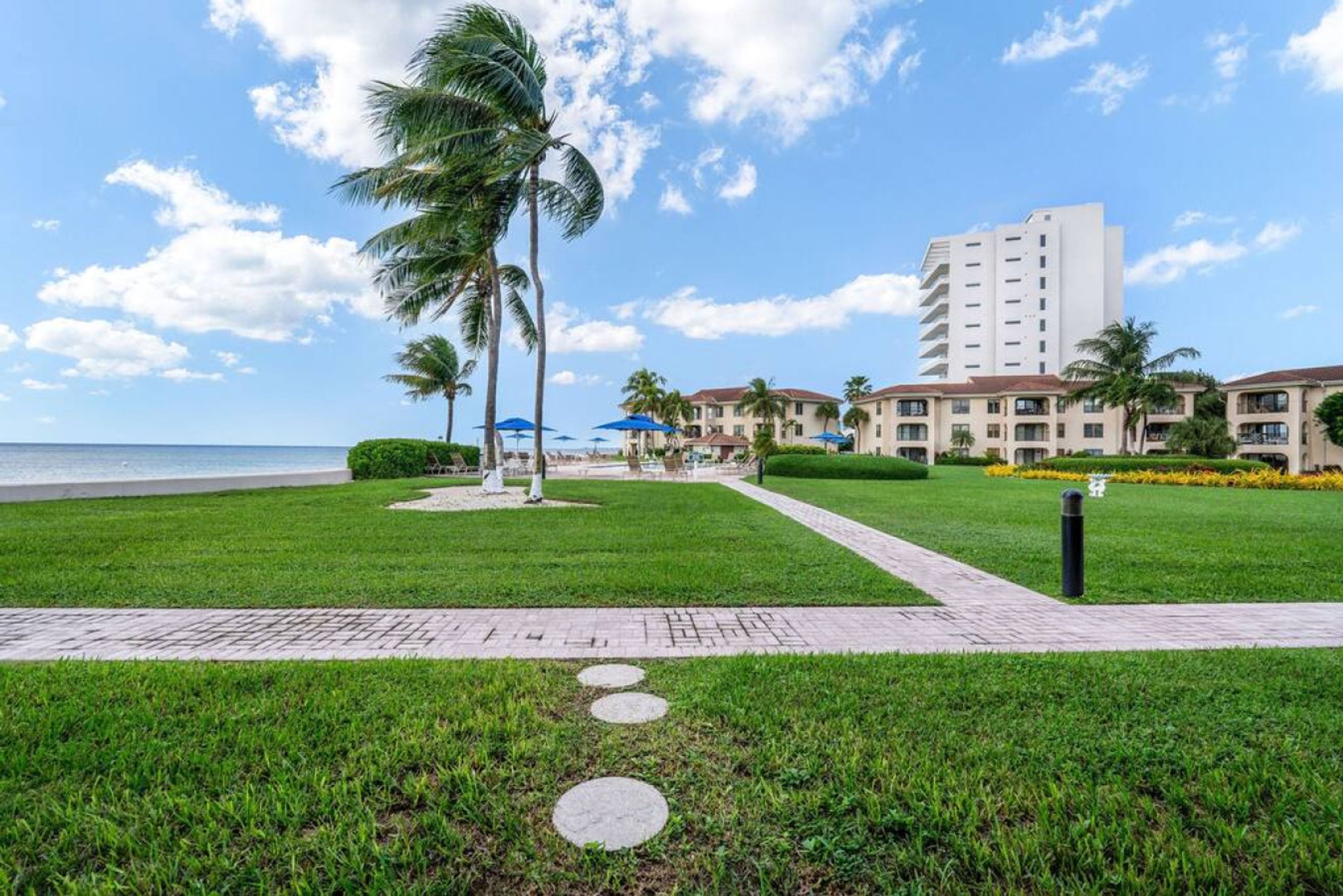 Un resort con un camino pavimentado, palmeras y edificios frente a la playa.