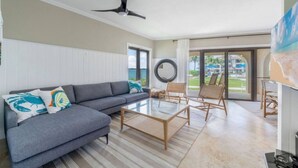 Ein modernes Wohnzimmer mit grauem Sofa, einem Glastisch, Korbstühlen und einem Deckenventilator.