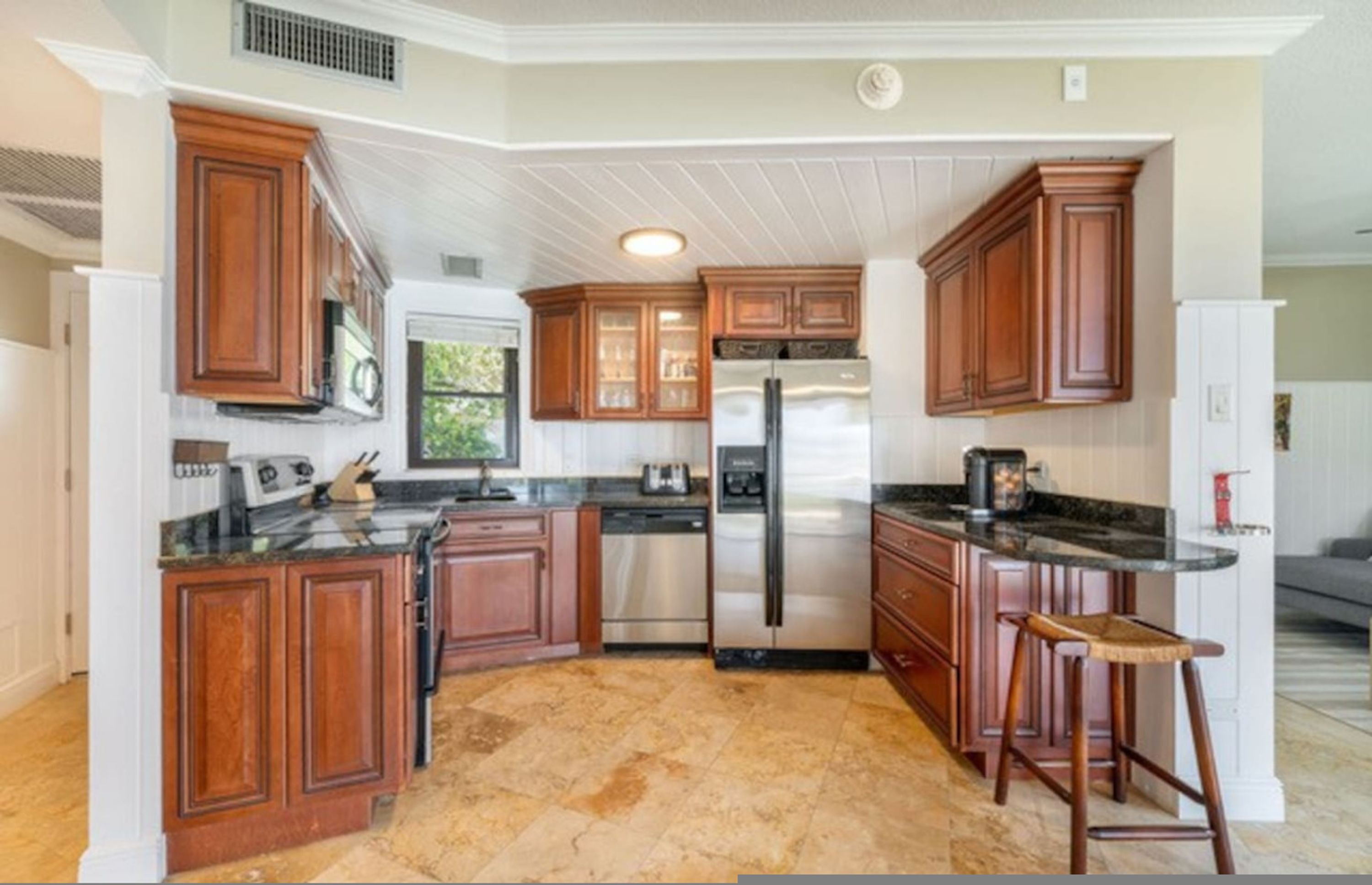 A kitchen with wooden cabinets, a stainless steel refrigerator, and a granite countertop.